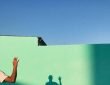 person waving reflecting shadow on teal wall paint