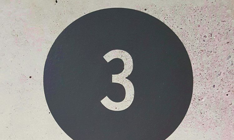 The number 3 against a dark grey circle on a grey wall